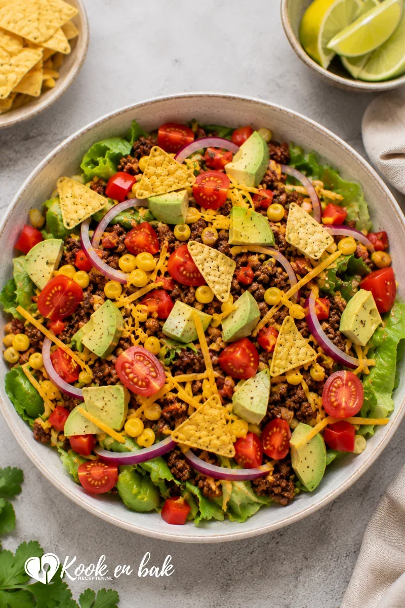 Kleurrijke Mexicaanse taco salade met gemengde sla, gekruid gehakt, maïs, cherrytomaten, rode paprika, avocado, rode ui, geraspte cheddar en knapperige tortillachips, geserveerd op een lichte ondergrond in natuurlijk daglicht.